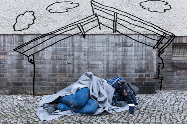 Homeless Male With Sign Sleeping Near Garbage And Rags