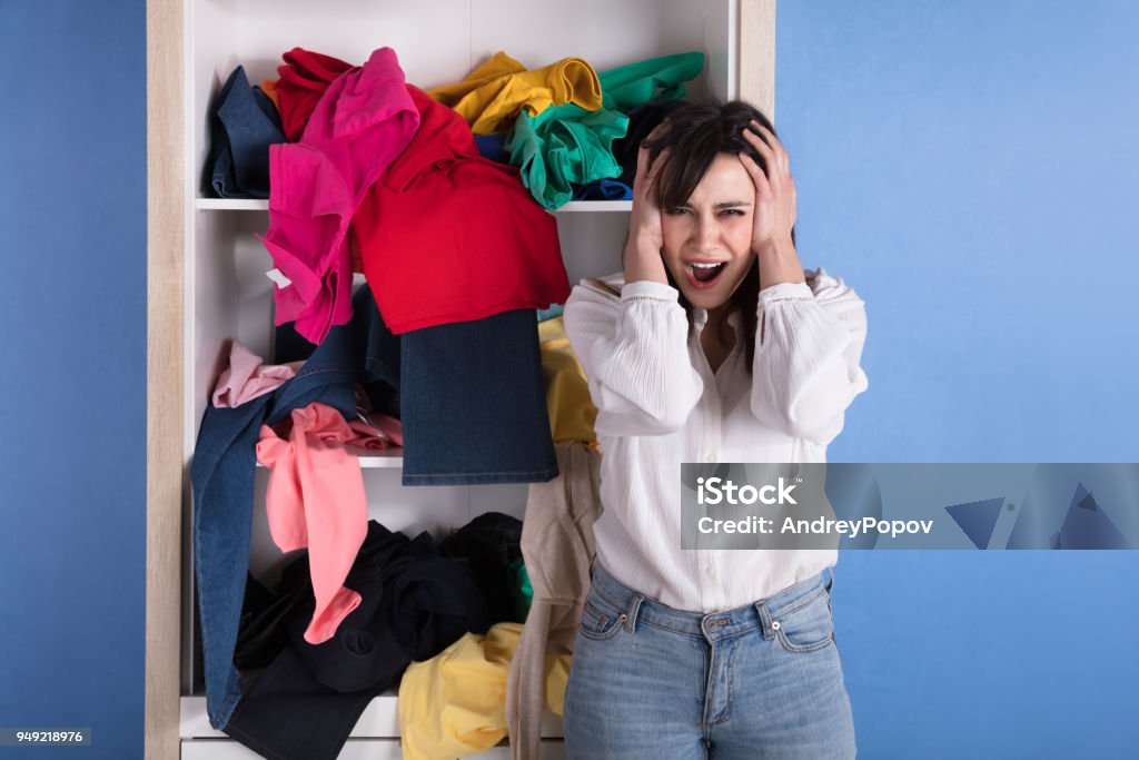 Portrait Of A Stressed Young Woman Portrait Of A Stressed Young Woman In Front Of Scattered Clothes On Shelf Closet Stock Photo