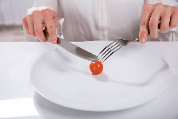 A Person's Hand Cutting Cherry Tomato On Plate With Knife And Fork