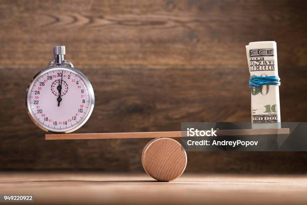 Closeup Of Stopwatch And Rolled Up Banknotes On Seesaw Stock Photo - Download Image Now