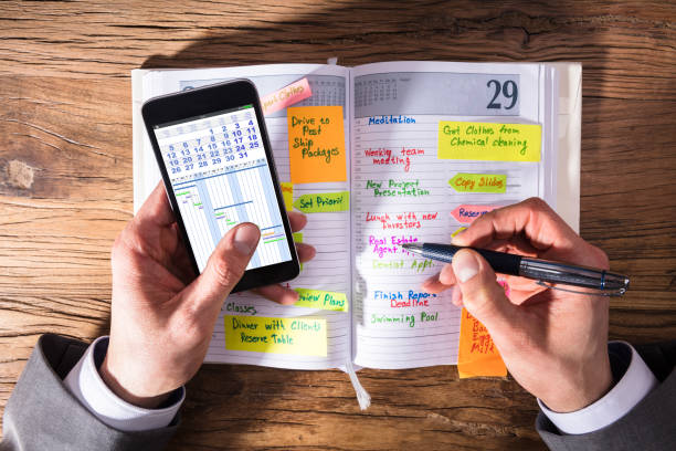 istock Businessperson With Mobile Phone Writing Schedule In Diary 949223144
