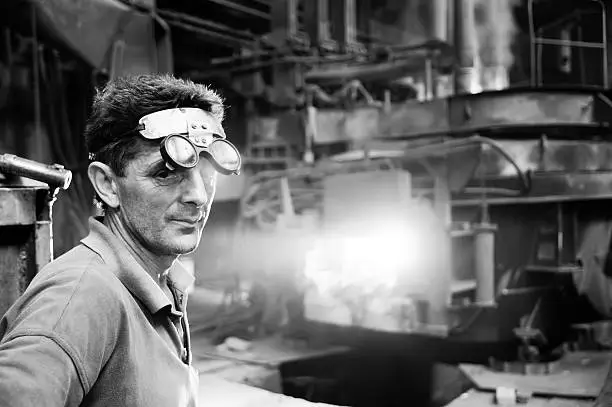 Worker standing in front of the electric arc furnace in steel mill. Black and white conversion.