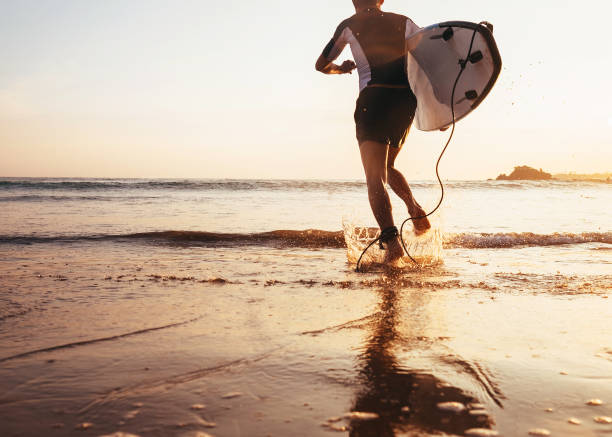 istock Man surfer run in ocean with surfboard in sunset light 949239038