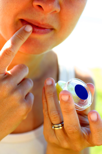A high key shot of a woman applying lip balm.