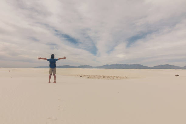 A young boy raises his arms to the sky during a hike at the White Sands National Monument in New Mexico, USA. He is feeling the great sense of wonder at the great sand dunes.