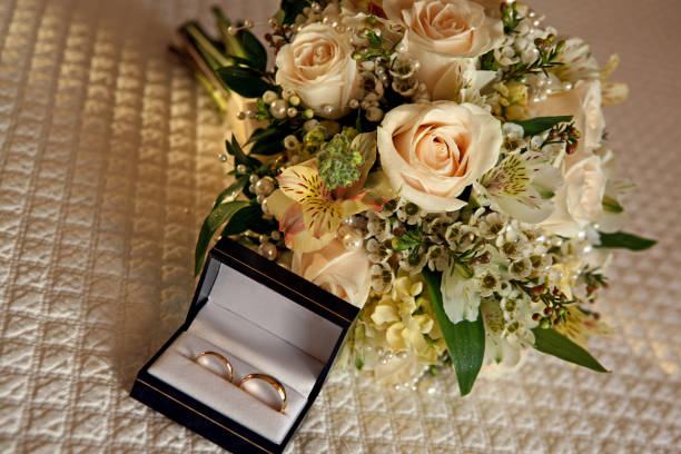 alianças de casamento em uma caixa junto com o buquê que sobre uma cama - foto de acervo