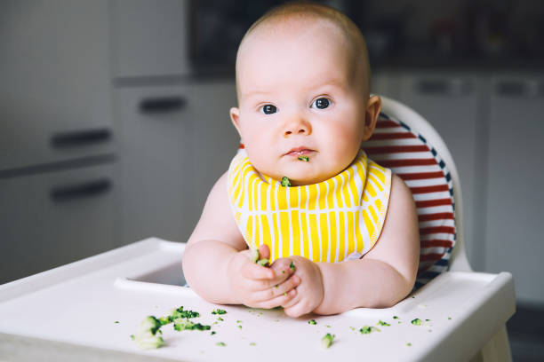istock Baby's first solid food. Feeding. Messy smiling baby eating with a spoon in high chair. 949265492