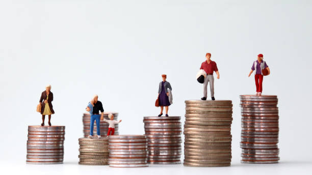 Miniature people standing on piles of different heights of coins. The concepts of person and wealth. stock photo