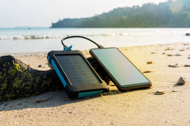 Portable solar panel is on the beach Portable solar panel is on the beach in the sand and charges the battery of the mobile phone. use of solar energy in the wild on a desert island. Modern frameless smartphone battery charger photos stock pictures, royalty-free photos & images