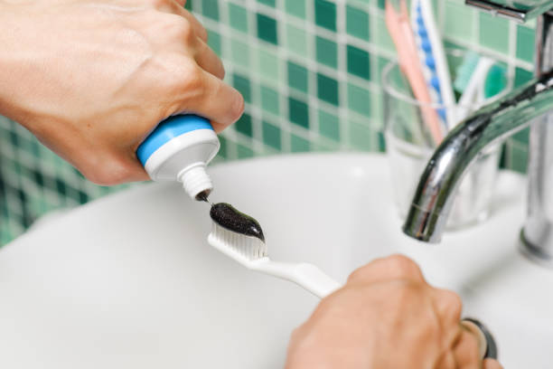 istock Close-up view of hands of woman squeezing black toothpaste 949302092