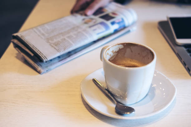 A detailed image showcasing a magazine page with vibrant imagery and text, a cup of coffee in a black saucer, and the woman's hand visible, indicating interest.
