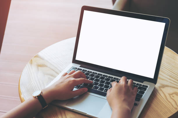 istock Mockup image of a woman's hands using laptop with blank white screen on wooden table in modern loft cafe 949307420
