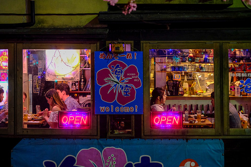 Young people enjoying food and drinks in an old fashioned bar in Kyoto's nightlife district not far from the Kamo river downtown. Viewed from the street outside.