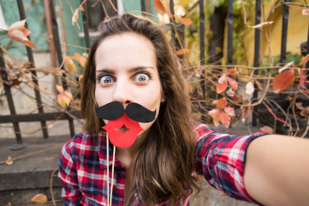 Mustache selfie Girl making a selfie with fake moustaches and lips at the sidewalk bench women movember mustache facial hair stock pictures, royalty-free photos & images
