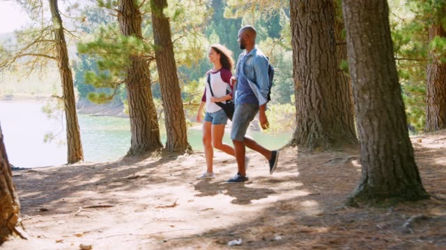 Couple On Countryside Hike Walking Through Woods By Lake