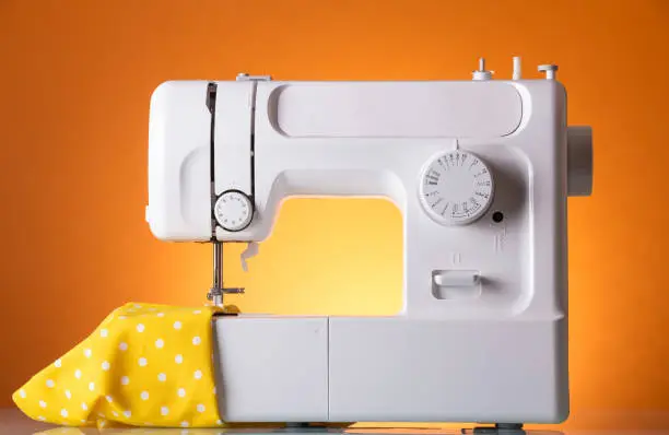 Household electric sewing machine in work, on bright-orange background