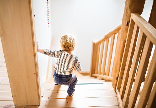 Little toddler walking down the stairs. Domestic accident. Dangerous situation at home. Child safety concept. Rear view.