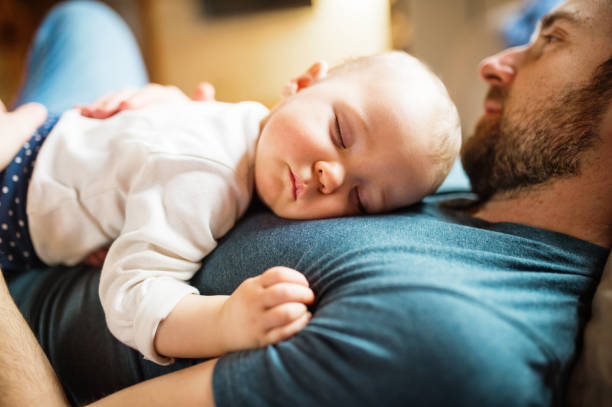 Father with a baby girl at home sleeping. Father with a baby girl at home, sleeping on the sofa. Paternity leave. Close up. genderblend stock pictures, royalty-free photos & images