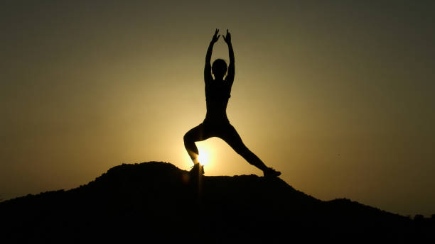 istock Silhouette of young woman enjoying harmony with nature while practicing yoga 949366322