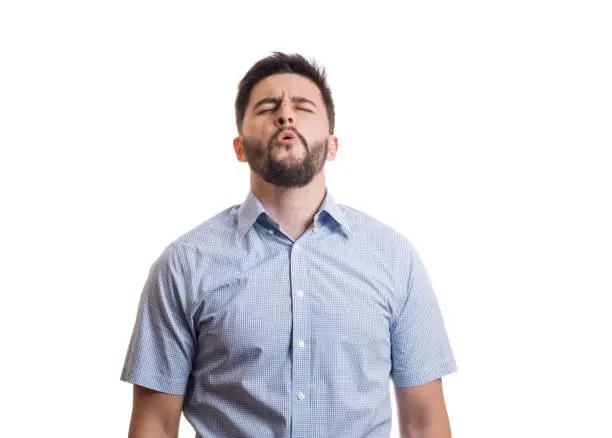 Young black haired guy with beard in blue casual shirt howling with closed eyes isolated on white background