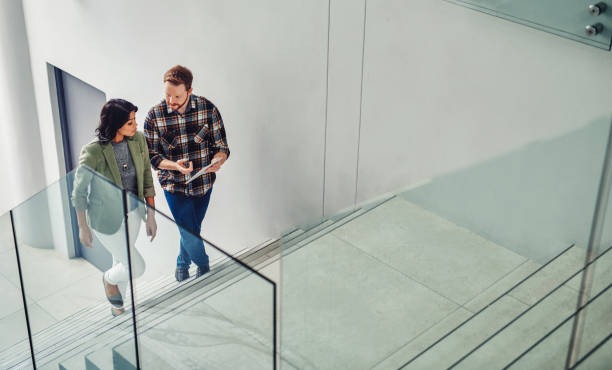 Putting business in motion Shot of two young coworkers using a digital tablet while walking up stairs in a modern office walking steps stock pictures, royalty-free photos & images