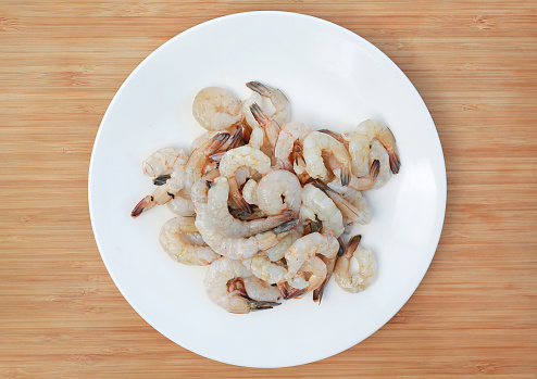 Raw shrimps in white plate on wooden background.