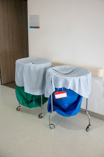 A pile of used clothes and infectious substances in hospital movable trolley with green bag and blue bag for laundry.