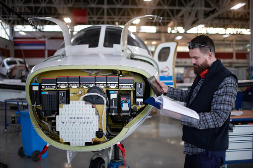 Male aircraft engineer in the hangar reading a manual before repairing private jet airplane.