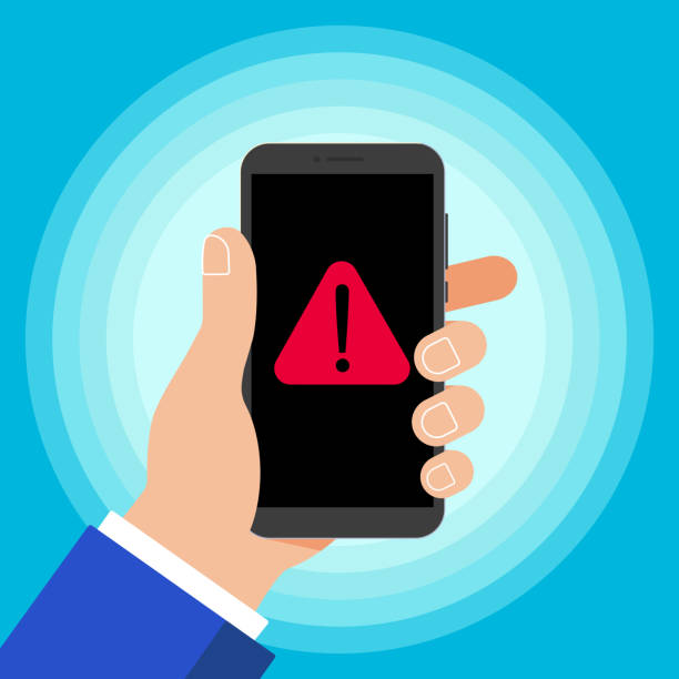 istock Hand holding black mobile phone with warning notice symbol icon sign on the screen isolated on background. Smartphone in human hand vector illustration flat design style. Attention, please! 949403888