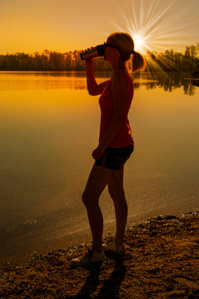 istock woman drinking outdoors from thermos bottle 949404312