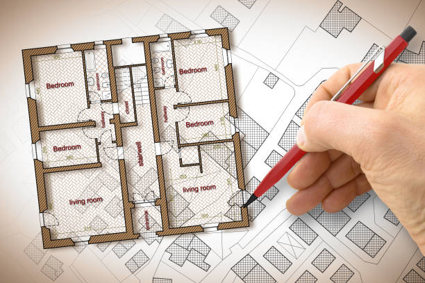 istock Architect drawing a residential building over an imaginary cadastral map of territory with buildings, fields and roads 949405252