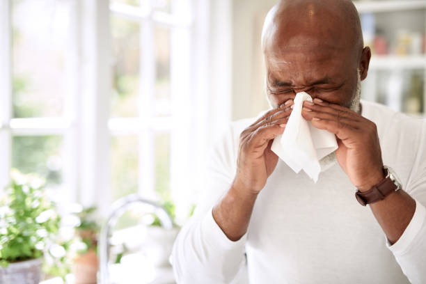 His immune system could use a boost Shot of a mature man blowing his nose at home sneezing stock pictures, royalty-free photos & images