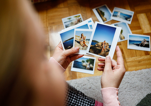 Young woman is browsing polaroid images from yesteryear summer vacation she spent with family in Greece. Authentic moments, original photographs.