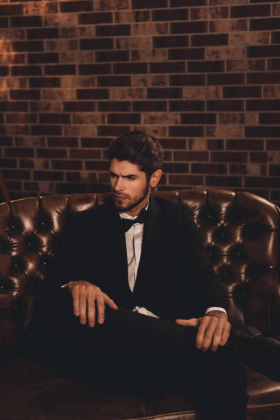 istock Imposing young man in elegant black suit sitting on couch 949430390