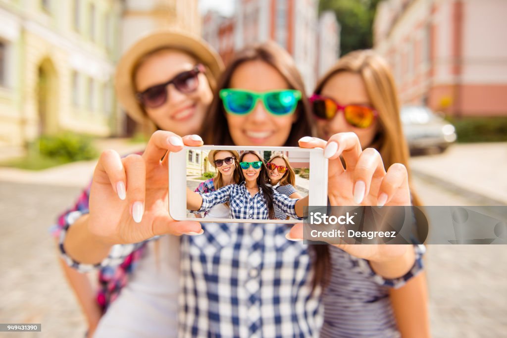 Three happy best girlfriends in glasses making selfie on smartphone Selfie Stock Photo