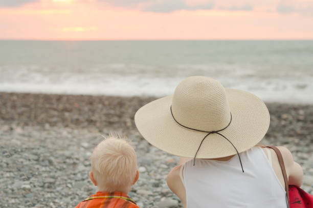 istock Mom and son rest on the pebble beach. Sunset time. Back view 949436386