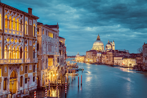 Classic view of famous Canal Grande with historic Basilica di Santa Maria della Salute in the background in beautiful mystic post sunset twilight with dramatic clouds in the sky at dusk, Venice, Italy