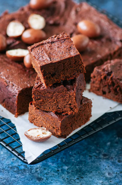 istock Dark chocolate brownie squares on a wire rack decorated with creamy chocolate eggs. Blue stone background. 949443400