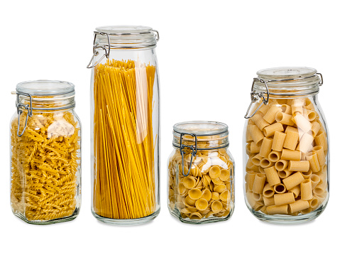 Photo of different pasta types in large glass jars over white background.