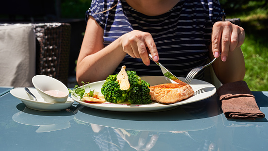 unrecognizable woman eating on terrace salmon and broccoli.