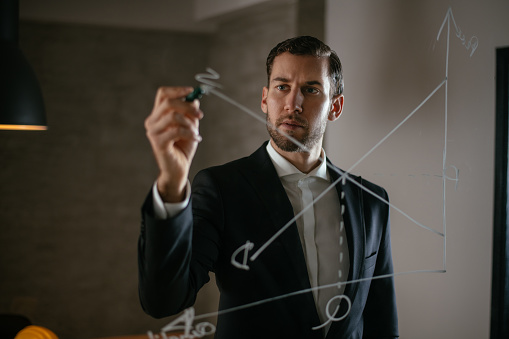 Businessman drawing graph on glass wall. Shallow DOF. Developed from RAW; retouched with special care and attention; Small amount of grain added for best final impression. 16 bit Adobe RGB color profile.