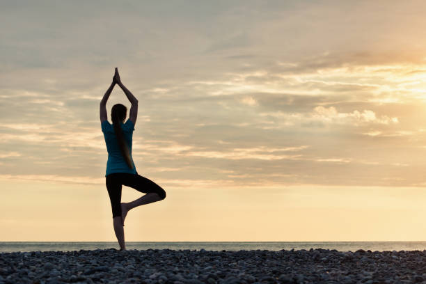 istock Girl at sunset practicing yoga at the seashore, back view 949451024