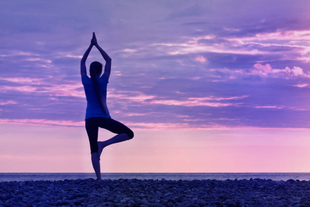 istock Girl at sunset practicing yoga at the seashore, back view 949451042