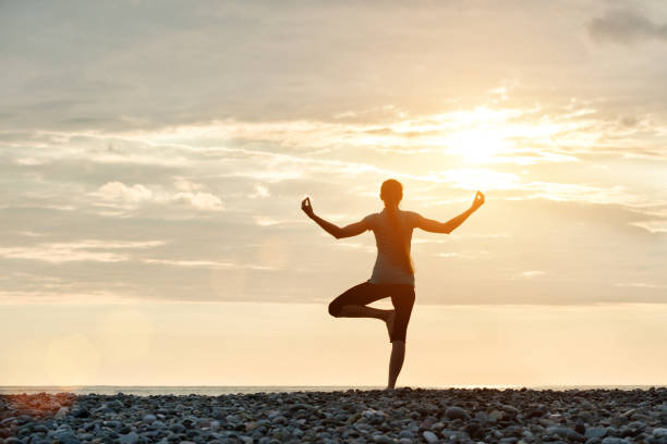 istock Girl at sunset practicing yoga at the seashore, back view 949451046