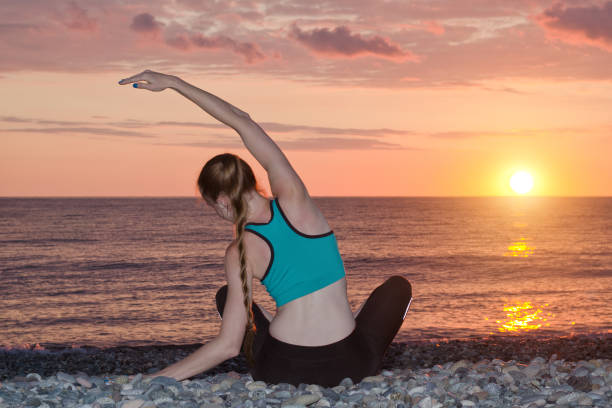 istock Girl practicing yoga on the beach. View from the back, sunset 949451088
