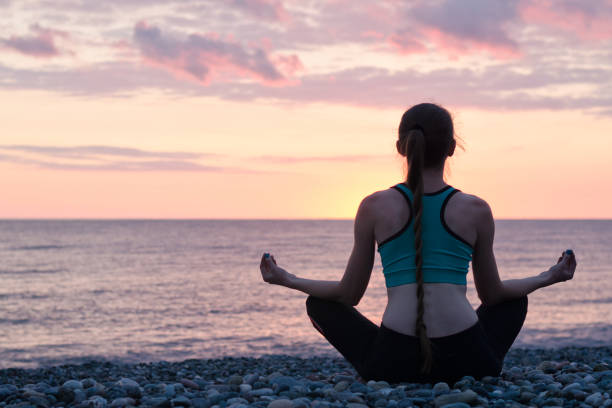 istock Woman meditating on the beach in lotus position. Sunset. Back view 949451116