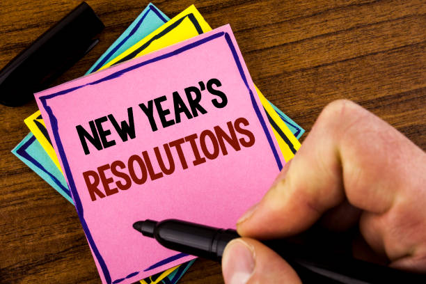 Word writing text New Year'S Resolutions. Business concept for Goals Objectives Targets Decisions for next 365 days written by Man Pink sticky note paper holding marker wooden background resoluciones de año nuevo de texto de la escritura de la palabra. concepto de negocio objetivos objetivos objetivos las decisiones para los próximos 365 días escrito por el hombre en el marcador de holding de papel nota adhesiva color rosa sobre fondo de madera