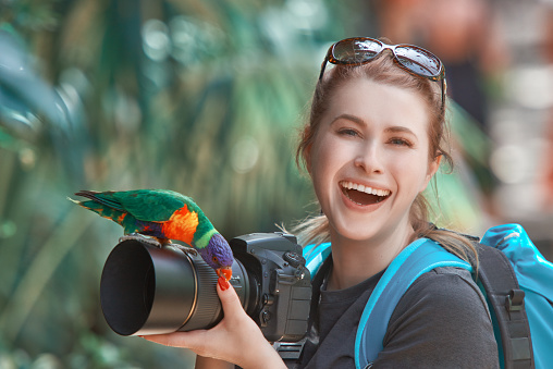 laughing photographer woman preparing to capture image, colorful parrot on her lens.