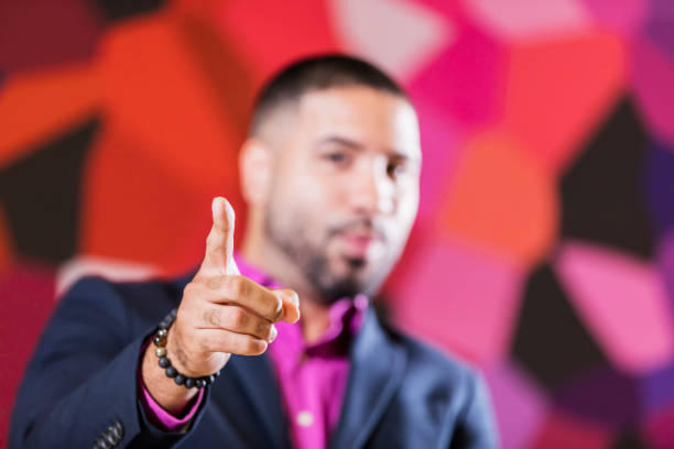 A mid adult mixed race Hispanic and African-American man pointing his index finger toward the camera. He is a businessman in a creative occupation, perhaps a designer or marketing professional. The focus is on his hand.