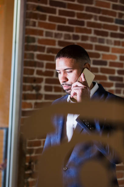 Businessman in booth talking on mobile phone A mid adult mixed race Hispanic and African-American man in his 30s with short hair, a beard and mustache, talking on his mobile phone, in a designated area for making telephone calls. pay phone on the phone latin american and hispanic ethnicity talking stock pictures, royalty-free photos & images